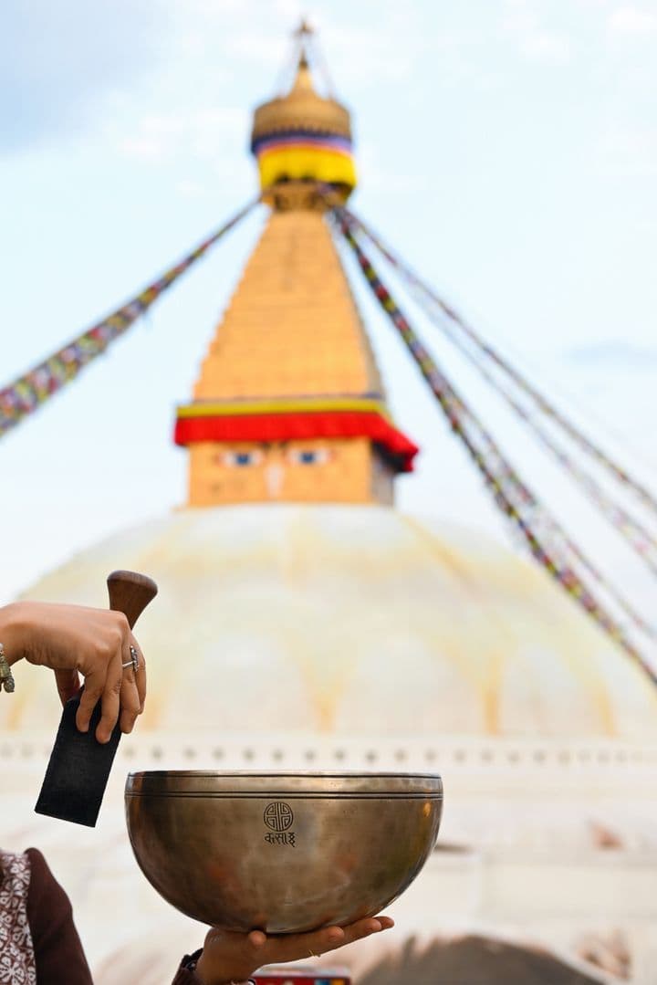 An engraved bronze singing bowl held before the Boudhanath stupa in Kathmandu