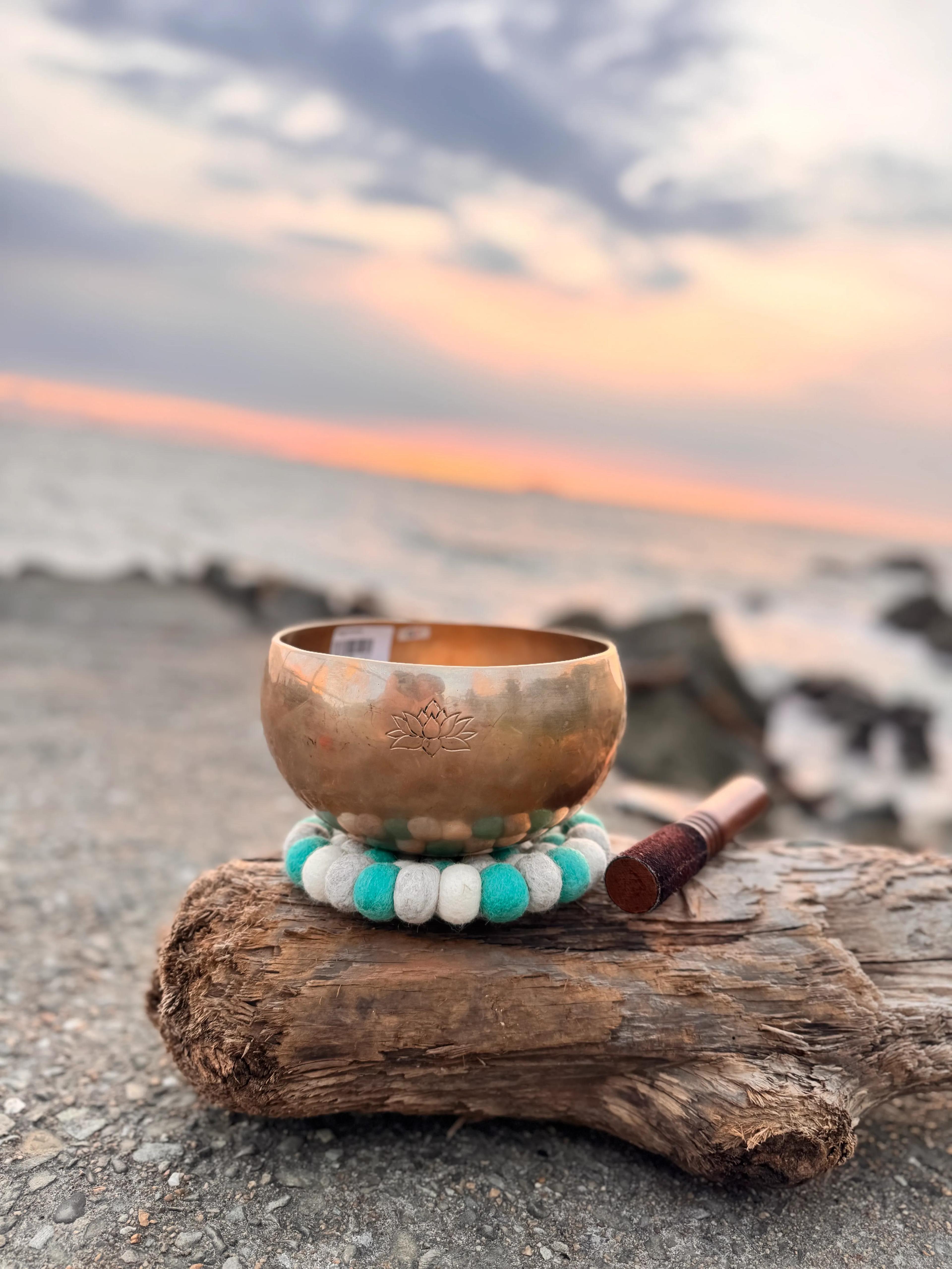 A practitioner sits cross-legged in meditation in a softly lit room, singing bowls on the mat before them